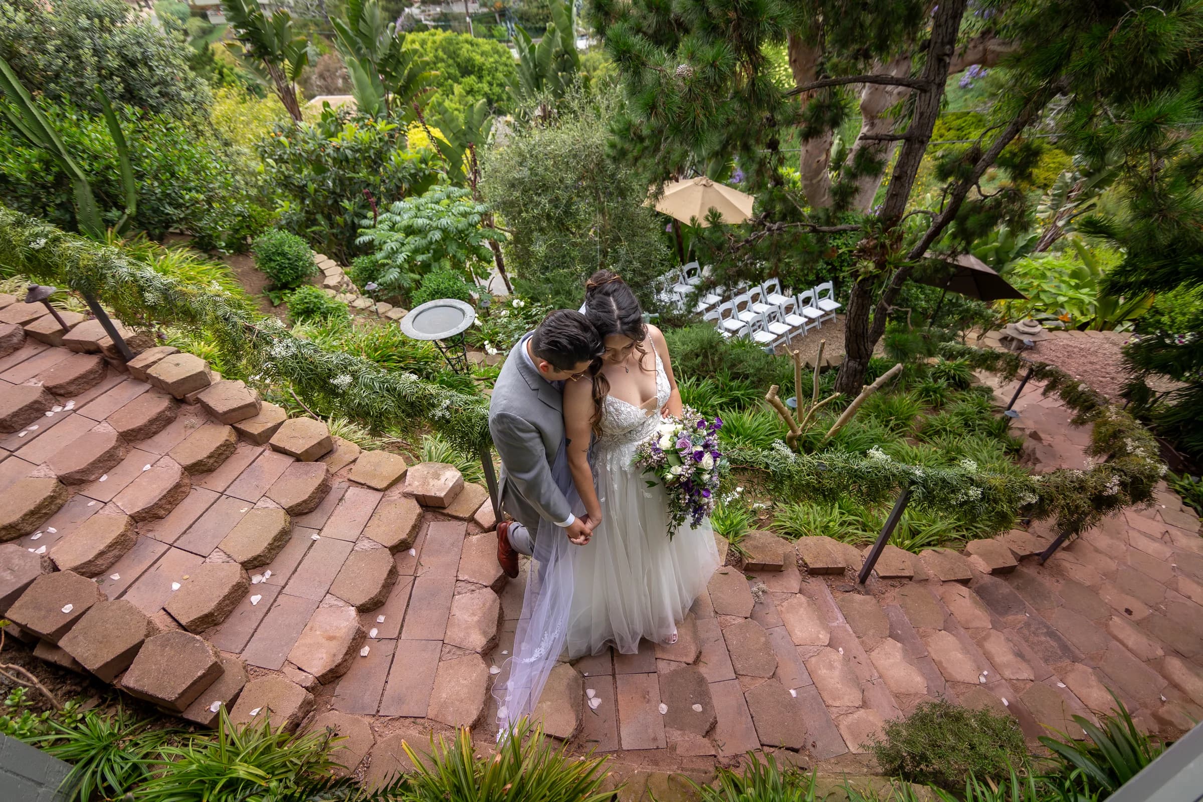 Newlyweds embrace on a garden staircase at their Del Mar wedding